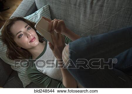 Picture - Caucasian woman laying on sofa texting on cell phone. Fotosearch