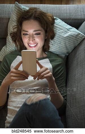 Stock Photography - Caucasian woman laying on sofa texting on cell phone. Fotosearch