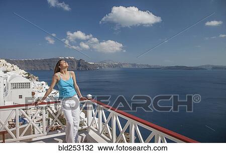 Stock Image - Caucasian woman leaning on balcony railing overlooking ocean. Fotosearch