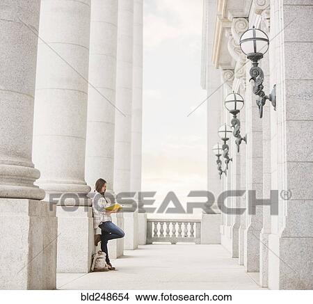 Picture - Caucasian woman leaning on pillar reading notebook. Fotosearch
