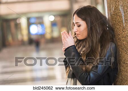 Stock Image - Caucasian woman leaning on pillar lighting cigarette. Fotosearch