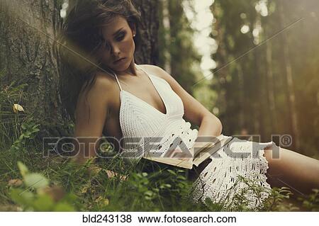 Stock Photo - Caucasian woman leaning on tree trunk reading book. Fotosearch
