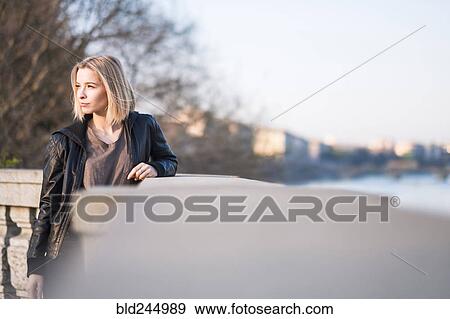 Stock Photo - Caucasian woman leaning on wall near river. Fotosearch