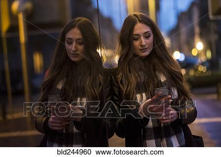 Stock Image - Caucasian woman leaning on window texting on cell phone outdoors. Fotosearch