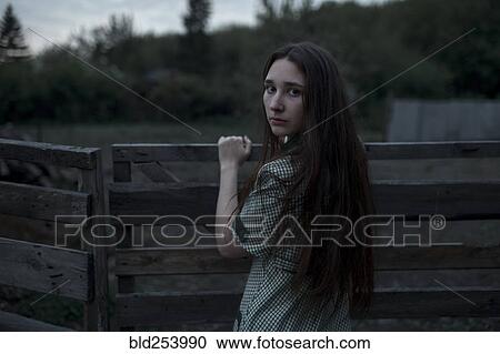 Stock Image - Caucasian woman leaning on wooden gate. Fotosearch