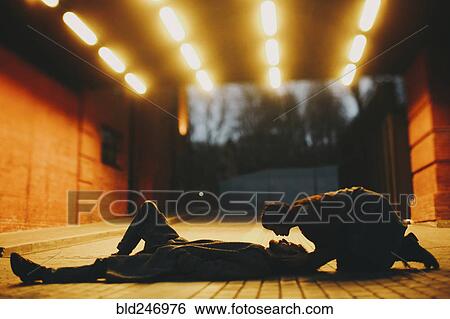Stock Photograph - Caucasian woman leaning over man laying on street in tunnel. Fotosearch