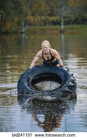 Caucasian woman lifting heavy tire in lake View Large Photo Image Stock Photo - Caucasian woman lifting heavy tire in lake. Fotosearch