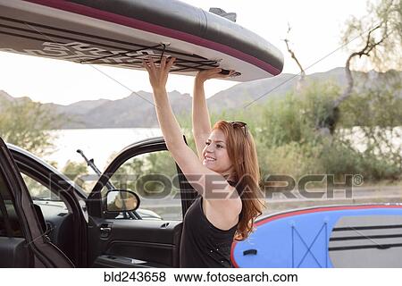 Stock Photo - Caucasian woman lifting paddleboard from roof of car. Fotosearch