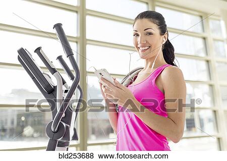 Stock Photo - Caucasian woman listening to cell phone in gymnasium. Fotosearch