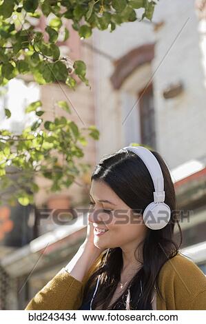 Picture - Caucasian woman listening to headphones in city. Fotosearch