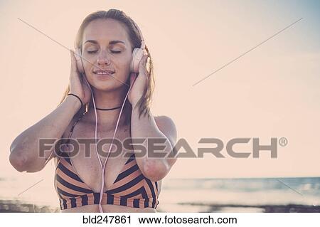 Stock Image - Caucasian woman listening to headphones on beach. Fotosearch