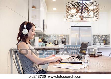 Caucasian woman listening to headphones reading paperwork using laptop View Large Photo Image Stock Photography - Caucasian woman listening to headphones reading paperwork using laptop. Fotosearch