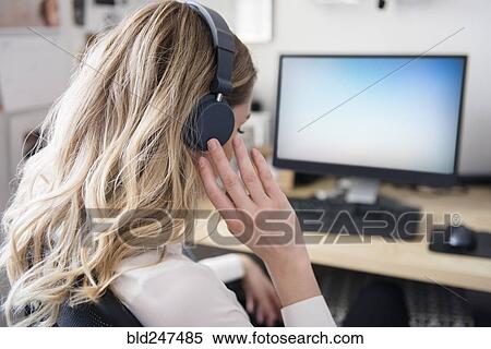 Caucasian woman listening to headphones at computer desk View Large Photo Image Stock Photography - Caucasian woman listening to headphones at computer desk. Fotosearch