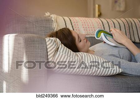 Stock Photograph - Caucasian woman napping on sofa holding book. Fotosearch