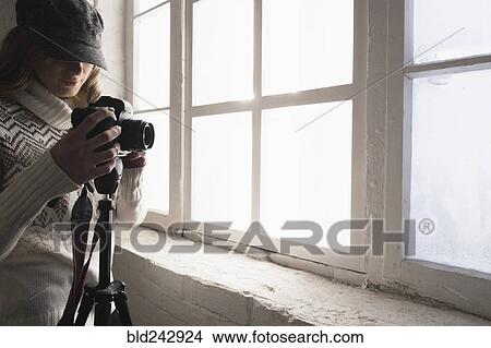 Picture - Caucasian woman near window photographing with camera. Fotosearch