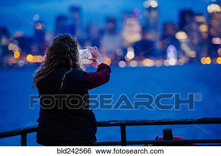 Stock Photograph - Caucasian woman on boat photographing urban waterfront with cell phone. Fotosearch
