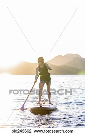 Stock Image - Caucasian woman on paddleboard in river. Fotosearch