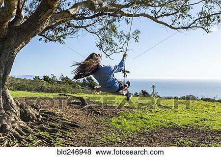 Stock Photo - Caucasian woman on tree swing near ocean. Fotosearch