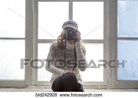 Stock Photo - Caucasian woman on window sill photographing with camera. Fotosearch