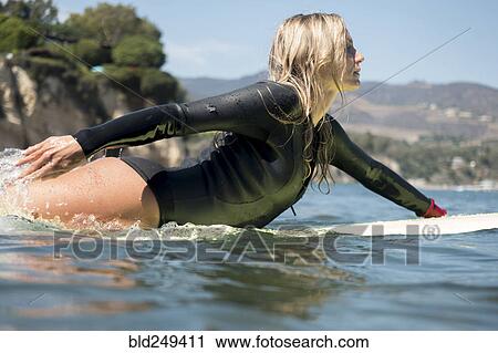 Stock Image - Caucasian woman paddling on surfboard in ocean. Fotosearch