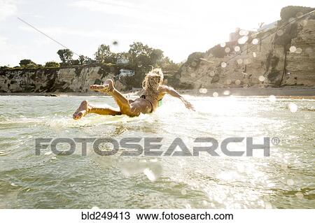 Stock Image - Caucasian woman paddling on surfboard in ocean. Fotosearch