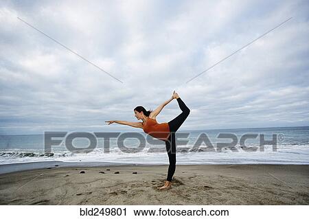 Stock Image - Caucasian woman performing yoga on beach. Fotosearch