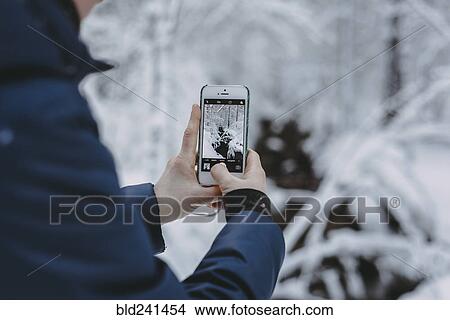 Picture - Caucasian woman photographing snow with cell phone. Fotosearch