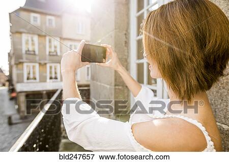 Stock Photo - Caucasian woman photographing with cell phone in city. Fotosearch