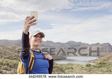 Stock Photo - Caucasian woman posing for cell phone selfie in desert. Fotosearch