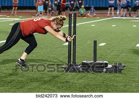 Stock Image - Caucasian woman pushing weight on sports field. Fotosearch