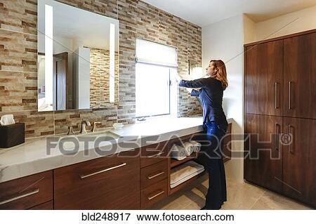 Stock Photo - Caucasian woman raising blinds on bathroom window. Fotosearch