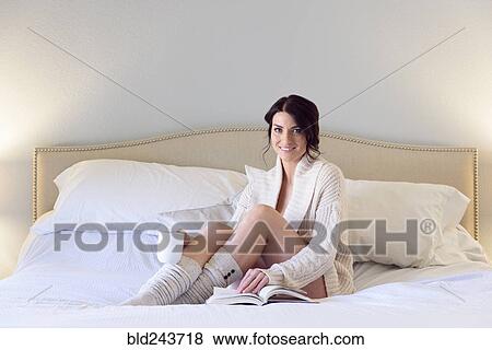 Stock Photo - Caucasian woman reading book on bed and drinking coffee. Fotosearch