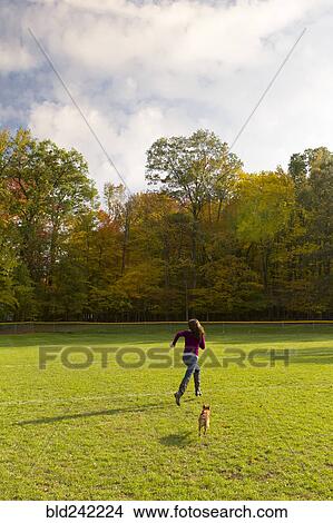 Picture - Caucasian woman running with dog in field. Fotosearch