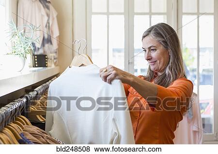 Stock Photo - Caucasian woman shopping at clothing store. Fotosearch