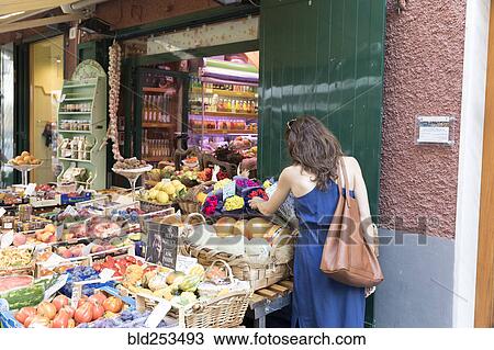 Stock Image - Caucasian woman shopping for fruit at sidewalk market. Fotosearch