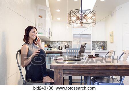 Caucasian woman sitting at table near laptop talking on cell phone View Large Photo Image Stock Photograph - Caucasian woman sitting at table near laptop talking on cell phone. Fotosearch