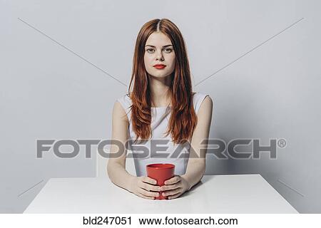 Caucasian woman sitting at table holding red cup View Large Photo Image Stock Image - Caucasian woman sitting at table holding red cup. Fotosearch