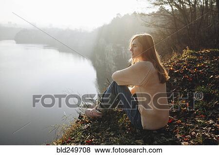 Stock Photo - Caucasian woman sitting at the edge of reservoir. Fotosearch