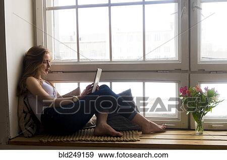 Stock Photo - Caucasian woman sitting at window using digital tablet. Fotosearch