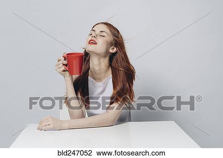 Stock Image - Caucasian woman sitting at windy table holding red cup. Fotosearch