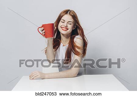 Stock Image - Caucasian woman sitting at windy table holding red cup. Fotosearch