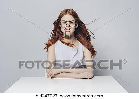 Stock Photo - Caucasian woman sitting at windy table with candy in mouth. Fotosearch