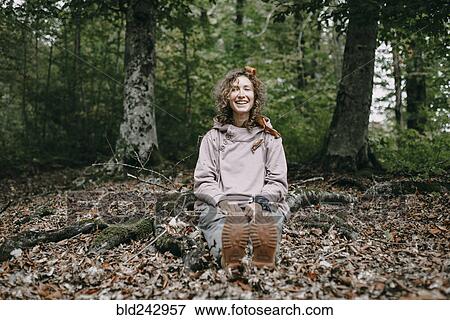 Stock Photo - Caucasian woman sitting in autumn leaves in forest. Fotosearch