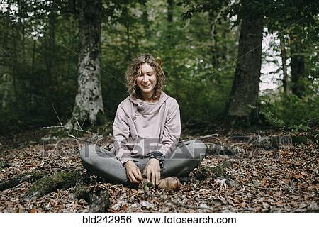 Stock Photograph - Caucasian woman sitting in autumn leaves in forest. Fotosearch