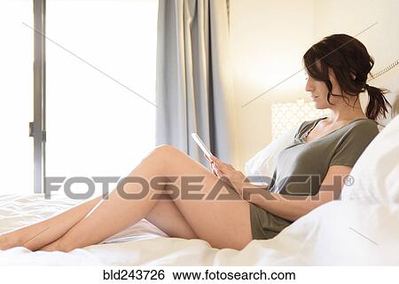 Stock Photograph - Caucasian woman sitting in bed using digital tablet. Fotosearch