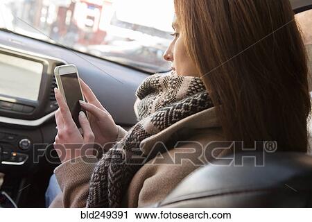 Stock Image - Caucasian woman sitting in car texting on cell phone. Fotosearch