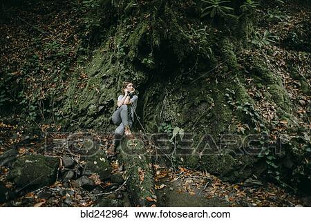 Picture - Caucasian woman sitting in forest holding branch. Fotosearch
