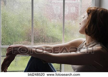Stock Image - Caucasian woman sitting near rainy window daydreaming. Fotosearch