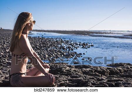 Stock Photo - Caucasian woman sitting on beach wearing bikini. Fotosearch