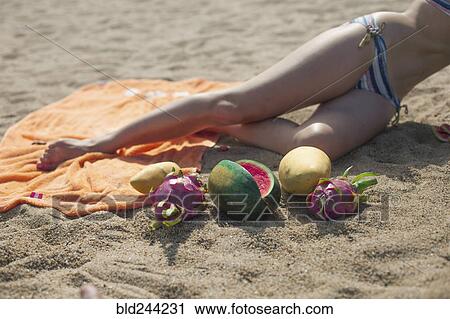 Stock Image - Caucasian woman sitting on beach with fresh fruit. Fotosearch